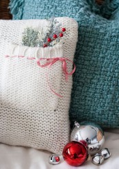 a lovely white knit pillow with a pocket and a plaid ribbon with a bow is perfectly styled for Christmas with evergreens and berries and looks very festive