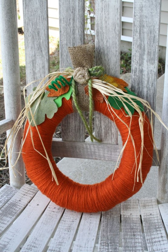 a colorful fall wreath covered with orange yarn, with colorful fall leaves, fabric blooms and husks