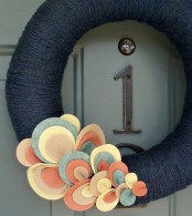 a contrasting fall wreath covered with black yarn and bright fabric leaves that decorate it