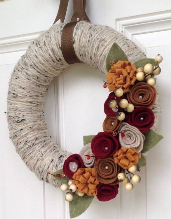 a fall yarn wreath covered with grey twine, with moody fabric flowers, leaves and faux berries for a more neutral look