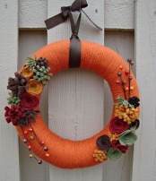 a colorful fall wreath with orange yarn, fabric blooms, berries and branches is a fun and playful idea