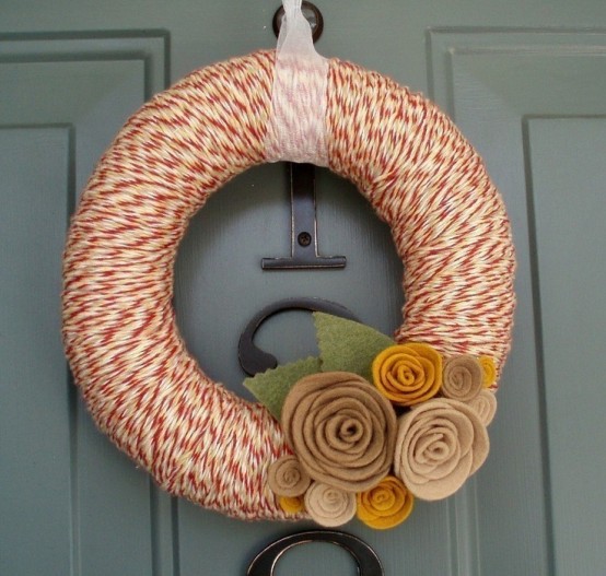 a bright yarn wreath covered with orange and white yarn for a pattern, fabric and burlap blooms and a ribbon