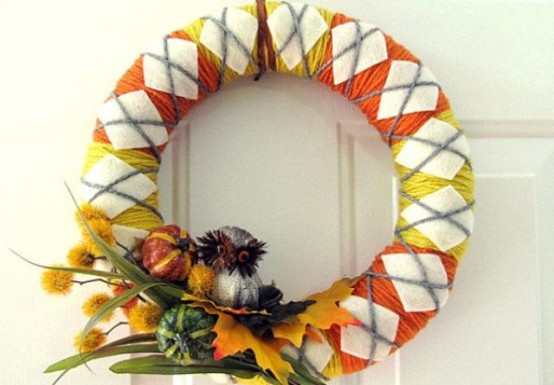 a colorful fall wreath with yellow and orange yarn, with white fabric rhombs, with faux leaves, veggies and dried blooms and a faux owl