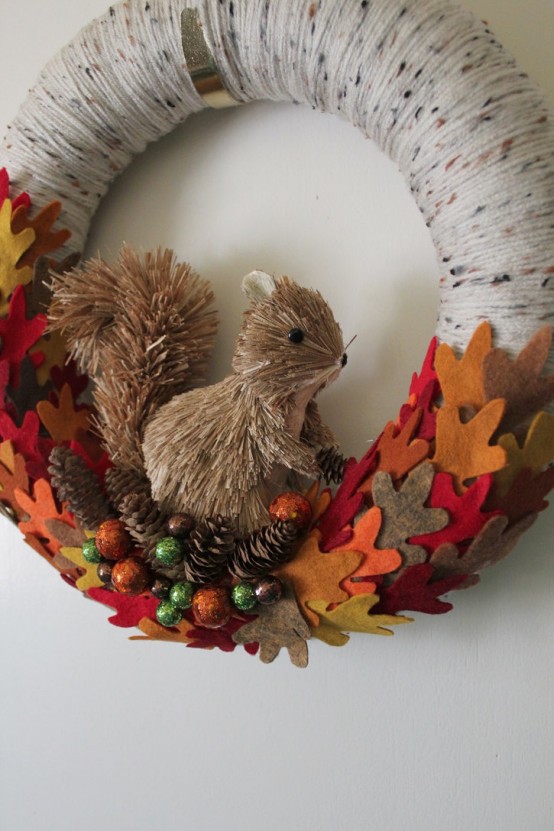 a bold fall wreath covered with grey yarn, with colorful fabric leaves, berries and a faux squirrel to add a woodland touch