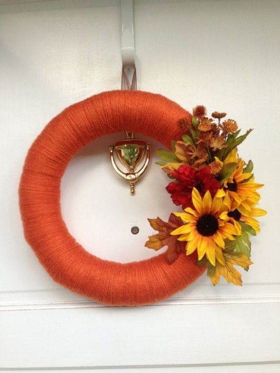 a bright fall wreath covered with orange yarn and with faux bold blooms and leaves and also dried flowers