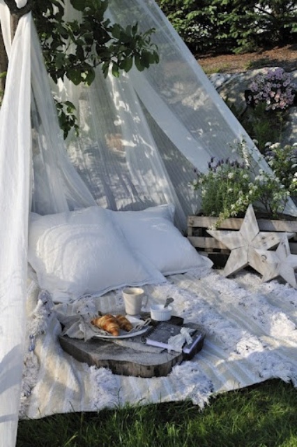 a cozy boho outdoor space done with a blanket, pillows and a mosquito net over the space