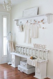 an all-white shabby chic entryway with a clothes hanger, a bench, some suitcases under the bench and some cute clothes