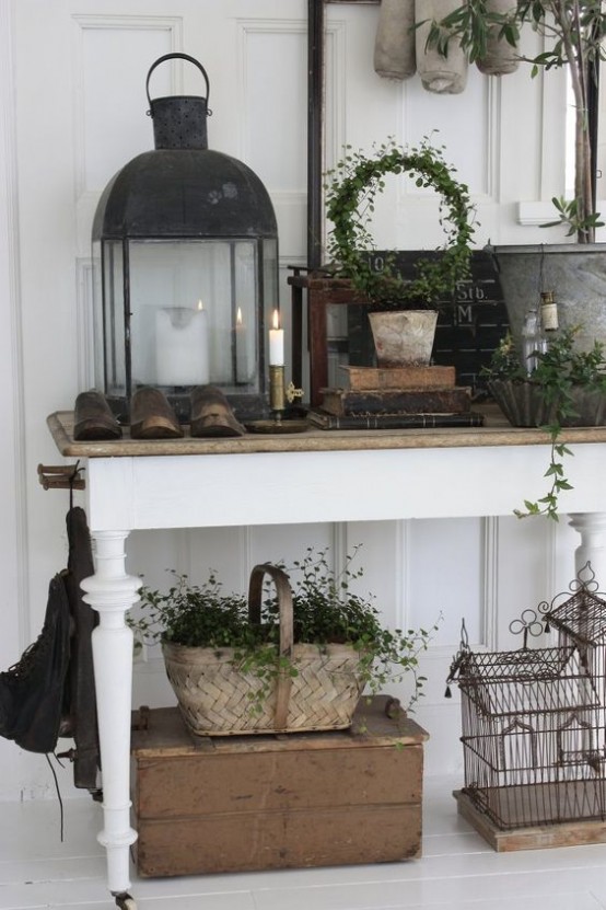 a shabby chic meets rustic entryway with a console table, boxes, candle lanterns, a basket and greenery all around