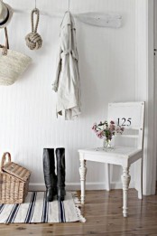 a beach meets shabby chic entryway with an oar as a clothes holder, a striped rug, a chair and a basket for storage