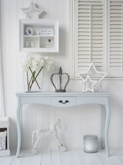 a cozy neutral shabby chic entryway with shutters, a pastel console table, a storage unit and a large candleholder