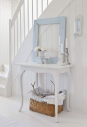 a white shabby chic entryway with an elegant console table, a blue frame, potted blooms and a basket for storage