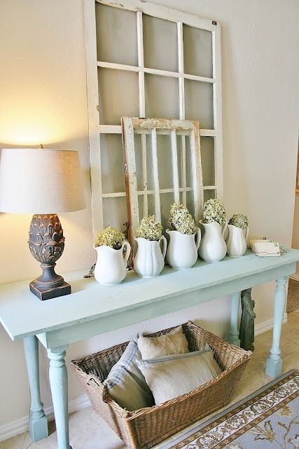 a shabby chic entryway with a powder blue console table, window frames, lamps and a basket under the table