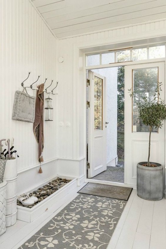 a neutral entryway with a pebble box for shoes, rugs, a potted tree and a clothes hanger