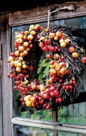 a fall twig and stick wreath with bright faux fruit is a fun and cool idea for autumnal outdoor decor