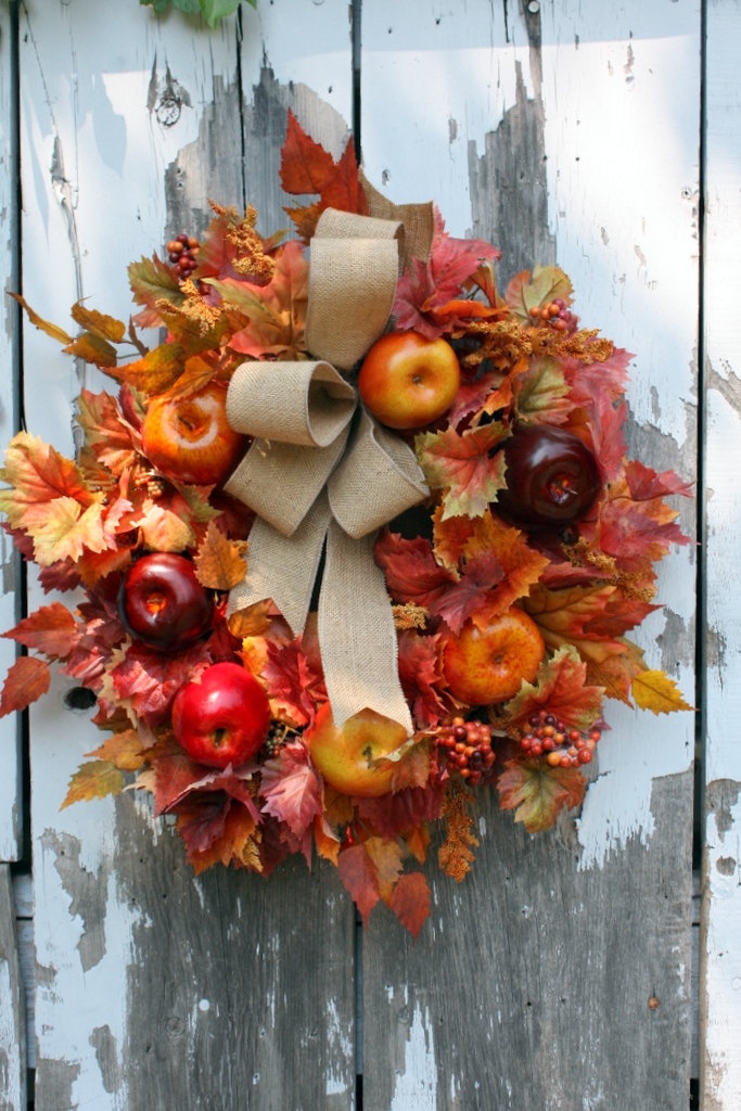 a bright fall wreath of faux foliage, bright apples and a burlap bow on top is a cool idea that will last long