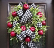 a bright and chic fall wreath of faux greenery, red apples and plaid irbbons and bows for cozy fall decor