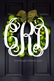 a bright fall wreath of faux green apples, evergreens, a green fabric bow and an oversized white monogram on top