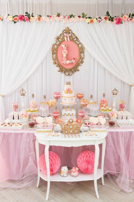a bright pink and peachy pink dessert table with fake florals, bright candies and sweets and a royal feel in decor