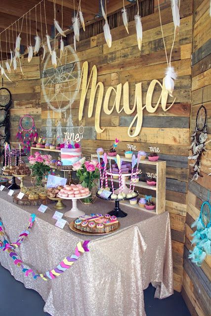 a super colorful dessert table done with purple, pink and turquoise touches, feathers, garlands and a dream catcher for a boho feel