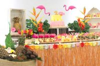 a tropical dessert table with touches of yellow, pink, green, orange, flamingos and fruits in a basket