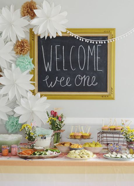 a bright dessert table styled with a framed chalkboard sign, paper flowers and pompoms and simple wildflower centerpieces
