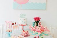 a colorful aqua and pink dessert table with flamingos, pink roses, a polka dot cake and a flamingo art piece