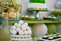 a green and white dessert table with various stands, trays and a sign over it