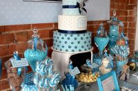 a turquoise and blue dessert table with lots of sweets displayed in jars, on plates, glasses and a large wedding cake on a stand