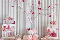 a pink and white baby shower table with vintage cages, a whitewashed tree with pink butterflies, vintage stands with various sweets