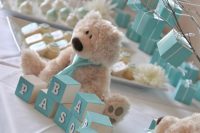 a boy’s baby shower dessert table decorated in turquoise, with turquoise cubes and a funny teddy bear