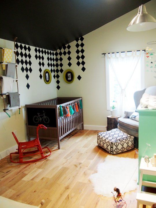 a boho black and white nursery with a dark IKEA Sundvik crib, a colorful tassel garland and a boho ottoman