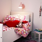 a small and cozy nursery with an IKEA Sundvik bed and colorful bedding and lamps