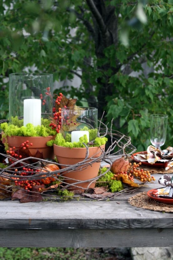 a fall woodland centerpiece of vine, moss, berries, dried blooms, planters with moss and candles