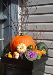 a natural outdoor fall arrangement of a large planter with pumpkins, gourds, blooms, cabbage and twigs and branches