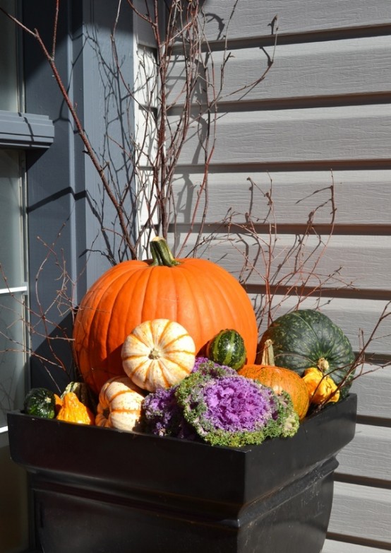 a natural outdoor fall arrangement of a large planter with pumpkins, gourds, blooms, cabbage and twigs and branches