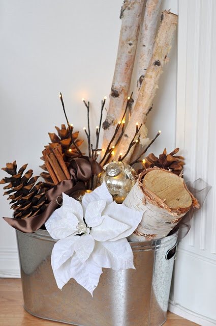 a fall to winter rustic arrangement with pinecones, cinnamon, tree stumps and branches, lights and white fabric blooms
