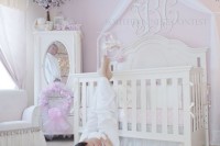 a vintage glam nursery with pink walls, vintage white furniture, a crystal chandelier and touches of pink