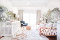 a neutral nursery with woodland murals on the walls, a white crib, a rattan sofa for parents, some pink touches and a blue chair