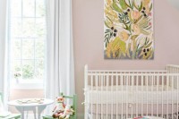 a pretty girlish nursery with pink walls, a wooden bead chandelier, a bright artwork and pastel kid’s furniture is cute