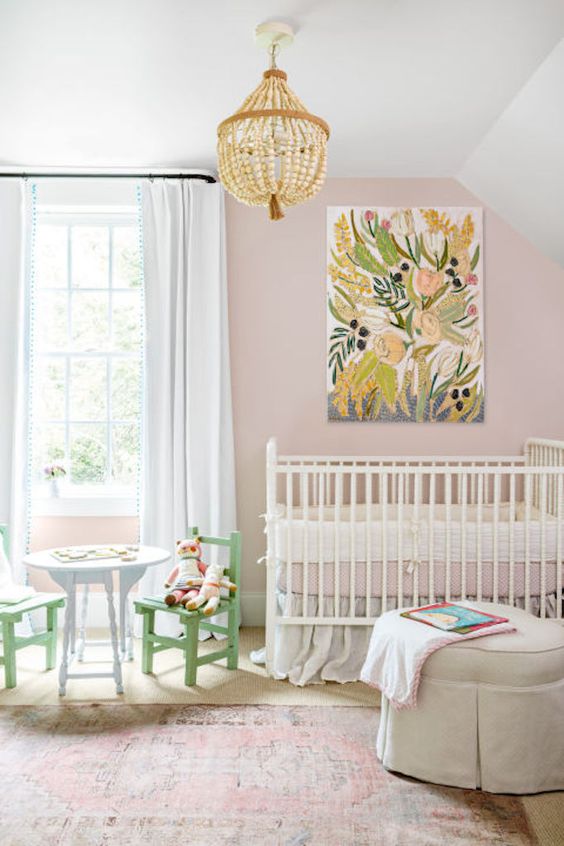 a pretty girlish nursery with pink walls, a wooden bead chandelier, a bright artwork and pastel kid's furniture is cute