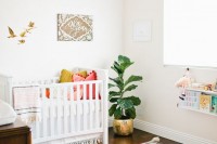 a bright and fun boho nursery with white and stained furniture, a leather ottoman, bright textiles and a statement plant in the corner