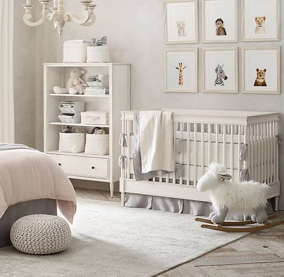 a neutral nursery with a fun gallery wall, white furniture, grey and pink bedding and a vintage chandelier