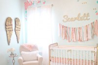 a pastel nurseru with mint walls, a vintage crib, a white chair and a gold ottoman, wings art on the wall and a tassel garland