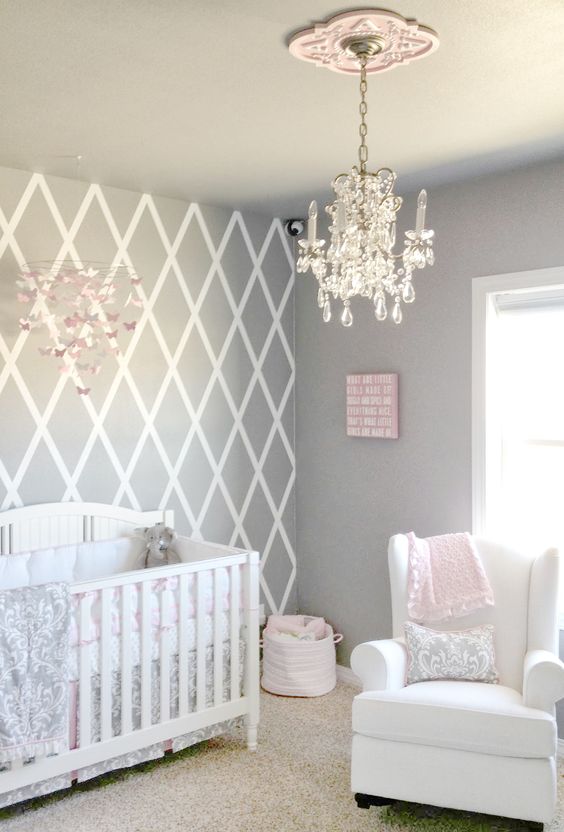 a pretty grey, white and pink nursery with white furniture, pastel bedding, a crystal chandelier and a paper butterfly mobile