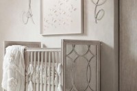 a vintage glam nursery in white and off-whire, with a vintage crib, a pretty artwork and rhinestone monograms plus a crystal chandelier