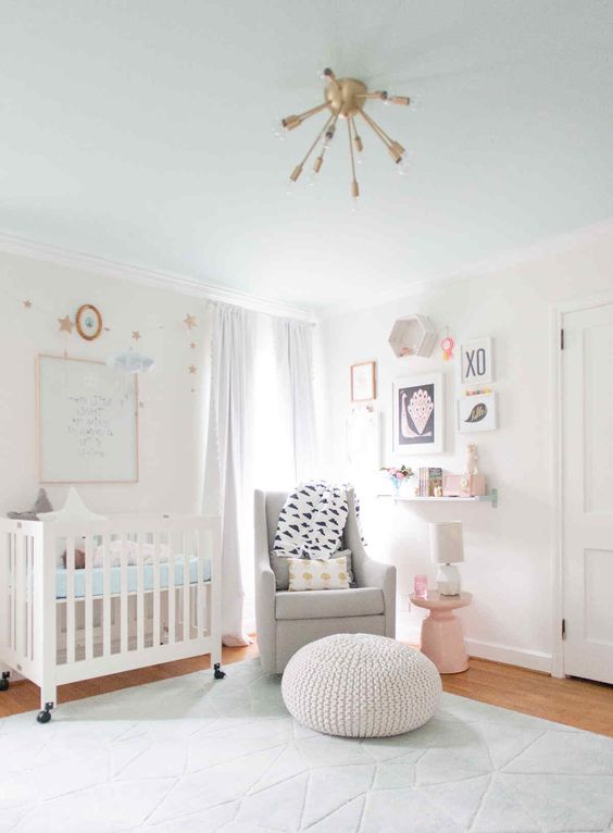 a peaceful white nursery with modern furniture, a grey chair and a pink side table, touches of brass and blue