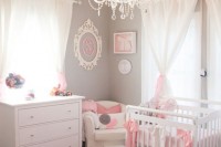 a girlish nrusery with grey walls, white furniture, pink and grey textiles, a crystal chandelier and art on the wall