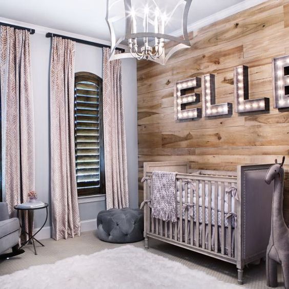 an eclectic nursery with a wood accent wall with marquee letters, shutter windows, pink curtains and a creative chandelier