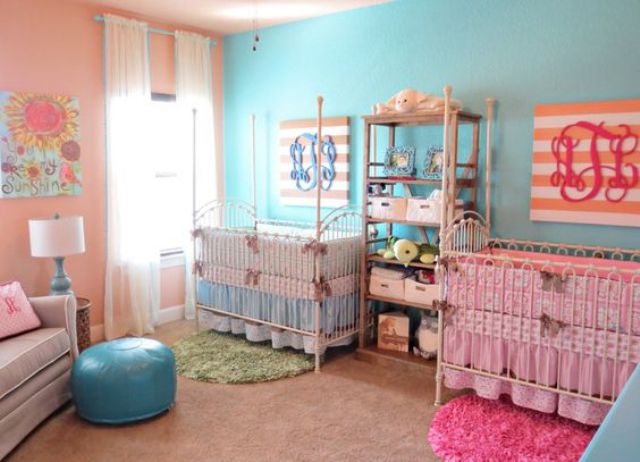 a colorful nursery with an accent pink and blue wall, with neutral furniture and a blue ottoman and various printed bright bedding