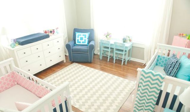 a neutral shared nursery with white and blue furniture and printed pink and blue linens plus a printed rug